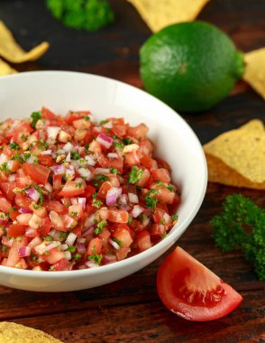 Limon, kırmızı soğan, jalapeno biber, maydanoz ve ahşap masada tortilla cips ile beyaz kapta Meksika Domates Salsa