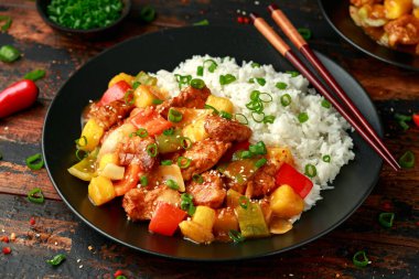 Ananas ve tavuk tatlı ve ekşi soslu dolmalık biber, pirinç ve ahşap masada taze soğan.
