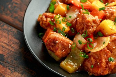 Tatlı ve ekşi soslu ananas ve tavuk ve siyah tabakta dolmalık biber.