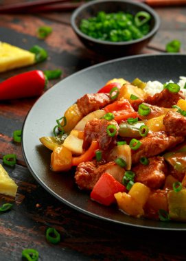 Tatlı ve ekşi soslu ananas ve tavuk yanında dolma biber, pirinç ve siyah tabakta taze soğan.