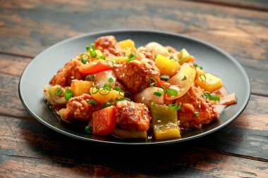 Tatlı ve ekşi soslu ananas ve tavuk yanında dolma biber, pirinç ve siyah tabakta taze soğan.