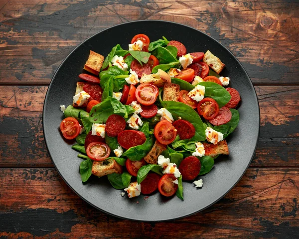 Салат из помидоров чоризо со шпинатом, сыром фета и гренками на черной тарелке. здоровое питание летом — стоковое фото