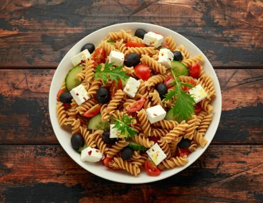 Domatesli makarna salatası, siyah zeytin, salatalık ve ahşap masada beyaz peynir. sağlıklı yiyecekler