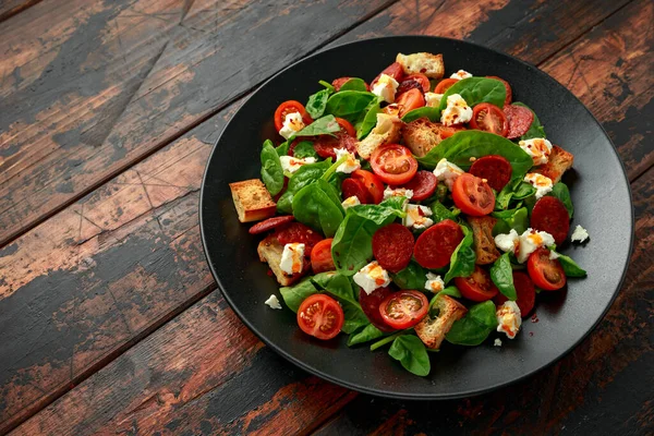 Салат з помідорами Чорізо зі шпинатом, сиром фета та грінками на чорній тарілці. здорове літнє харчування — стокове фото