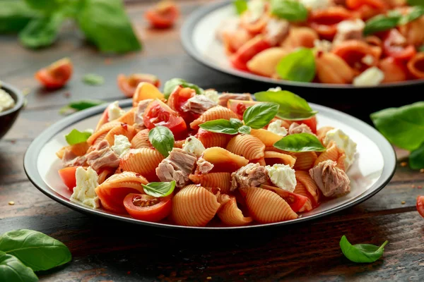 Conchiglie Tuna pasta with tomato sauce, feta cheese and basil on wooden table. healthy food