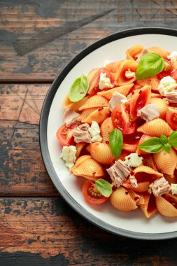 Domates soslu Conchiglie Tuna Makarnası, ahşap masada beyaz peynir ve fesleğen..