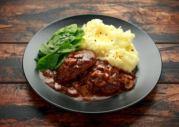 Salisbury Steak with mushroom gravy, mashed potatoes and spinach on rustic wooden table