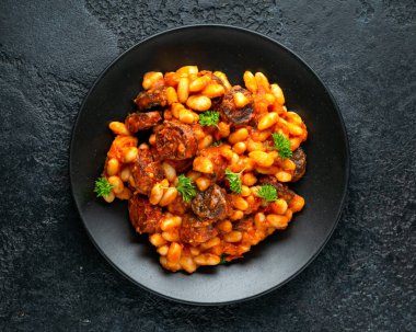 Siyah tabakta maydanozlu fasulye ve sucuk yahnisi.