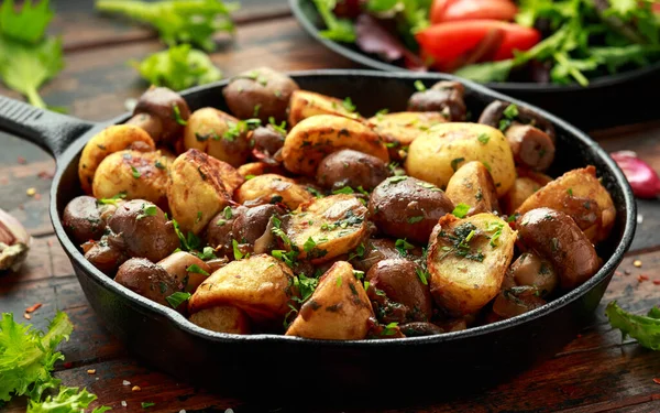 Patata al forno con funghi ed erbe aromatiche in padella di ghisa sul tavolo di legno — Foto Stock