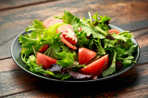 Salade de tomates fraîches avec légumes sur assiette noire. table en bois. aliments sains. — Photo