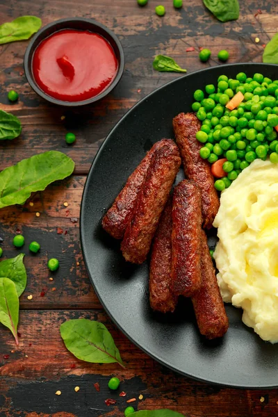 Salsichas vegetarianas vegan com purê de batata e ervilhas verdes em placa preta — Fotografia de Stock