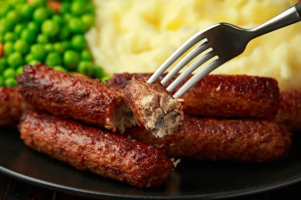 Vegetarian vegan sausages with mashed potato and green peas in black plate — Stock Photo, Image