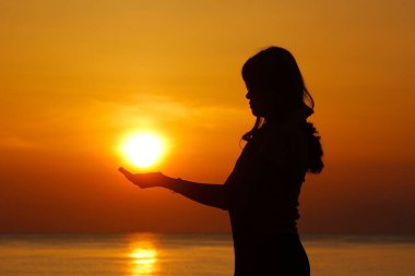 Kumsalda güneşi tutan kadın silueti.