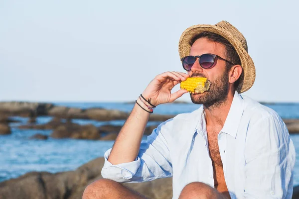 ビーチで若い男が食べるトウモロコシ — ストック写真