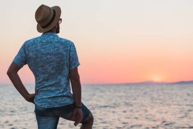 Genç adam deniz kenarında günbatımının tadını çıkarıyor.