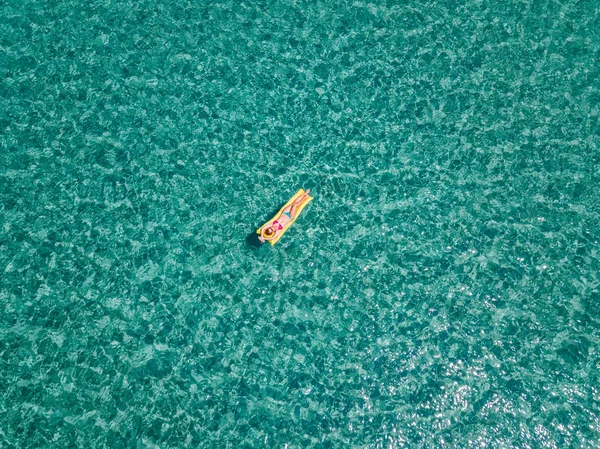 Aerial view of woman floating on the water mattress in the turquoise sea