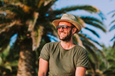 Güneşe bakarak palmiye ağaçları tarafından ayakta genç adam