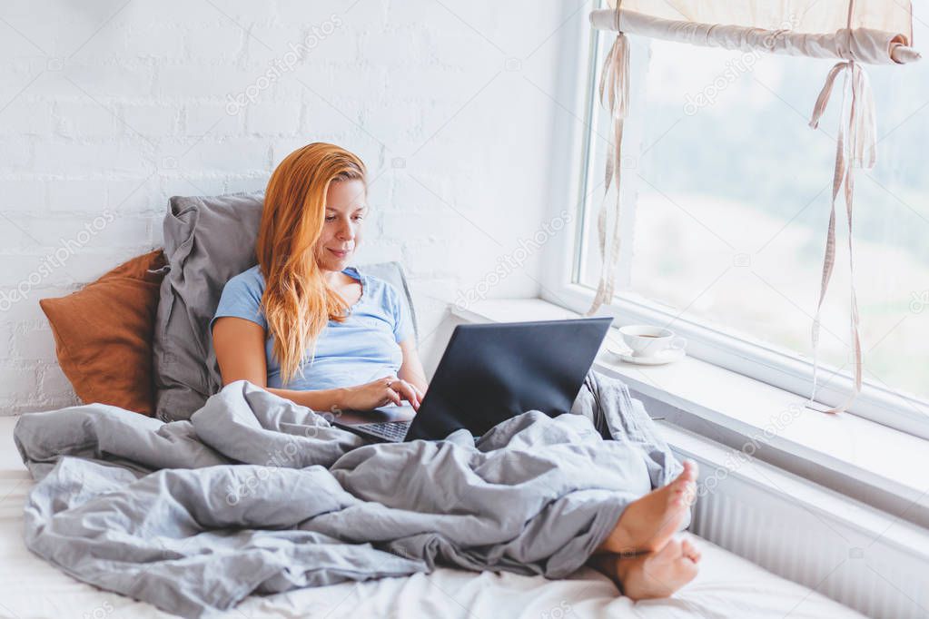 Woman working in bed on laptop early in the morning