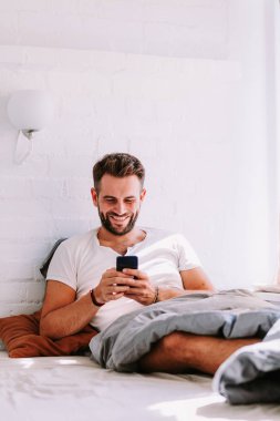 Sabahleyin yatakta Smartphone kullanan genç adam