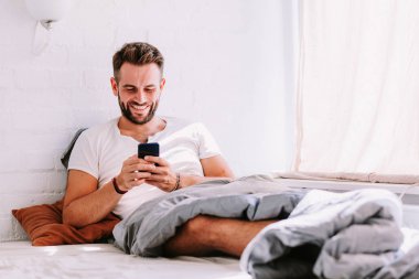 Sabahleyin yatakta Smartphone kullanan genç adam