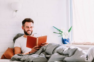 Genç adam yatakta kitap okuma
