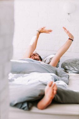 Young man waking up in the bed in the morning clipart