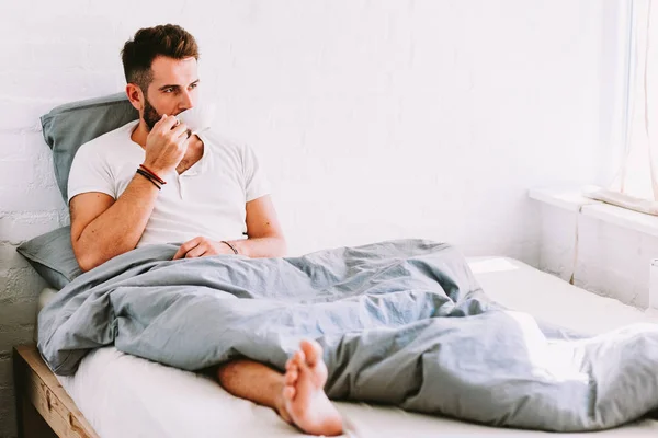 Young man drinking coffee in bed