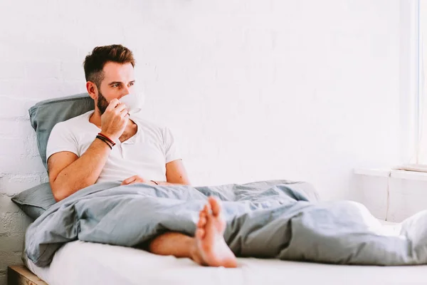 Young man drinking coffee in bed
