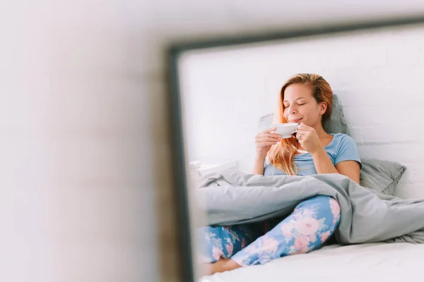 Young woman drinking coffee in bed