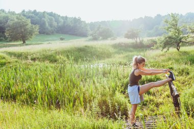 Genç kadının günbatımında doğa egzersiz yapması