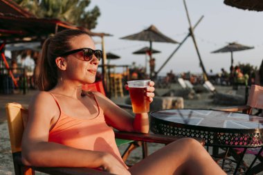 Genç kadın zevk günbatımı bar Beach bira içmek