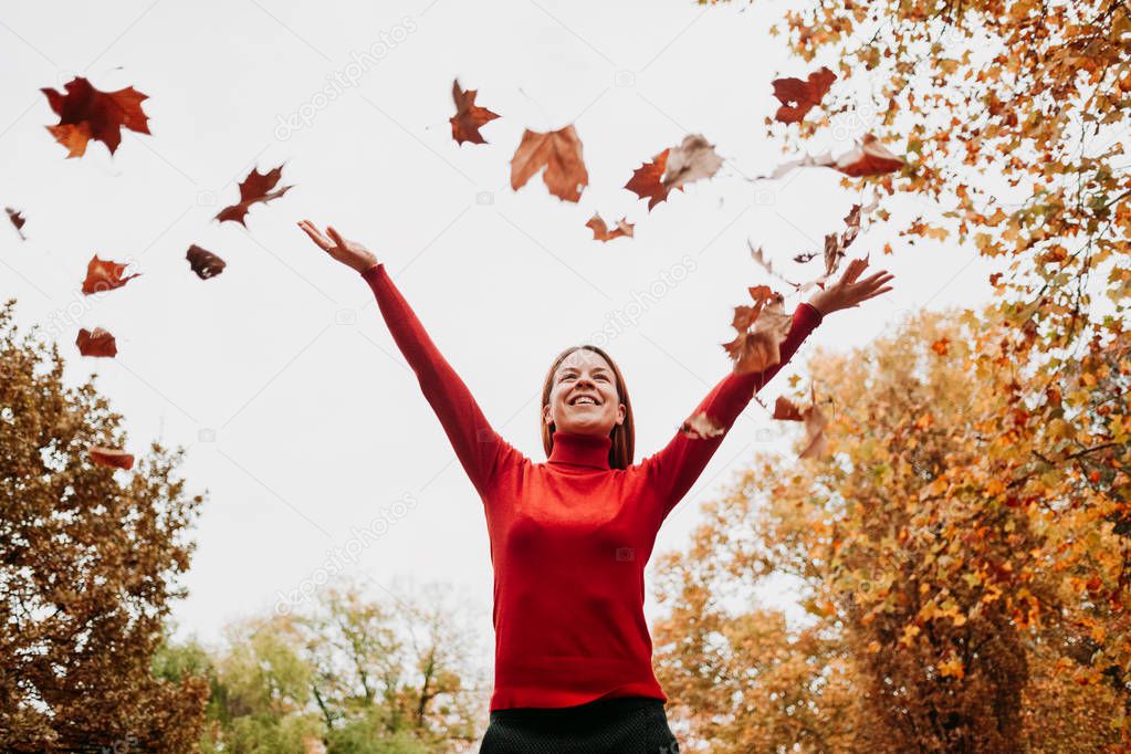 Young woman throwing autumn leaves in the air in the park