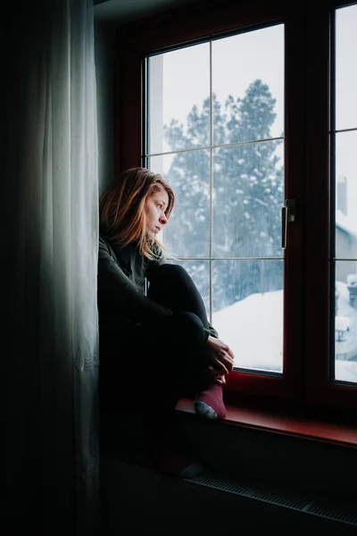 悲しい女性が外を見て窓辺に腰掛けて — ストック写真