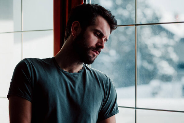 Bearded young man by the window in despair 