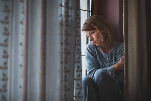 Sad woman sitting by the window looking outside