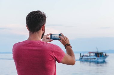 Turist alarak fotoğraf ile smartphone denizin kenarında genç adam