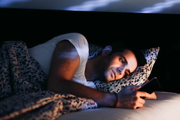 Young man using smartphone in bed at night