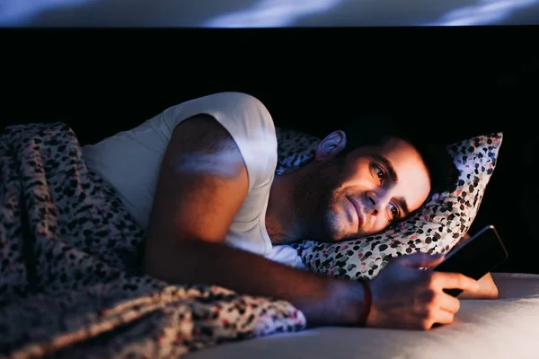 Young man using smartphone in bed at night