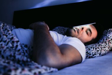 Geceleri yatakta Smartphone kullanan genç adam