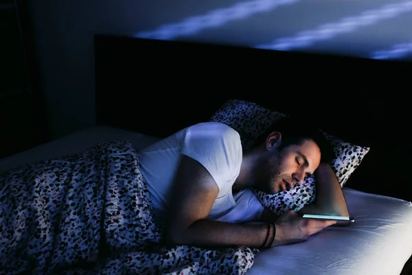 Young man using smartphone in bed at night