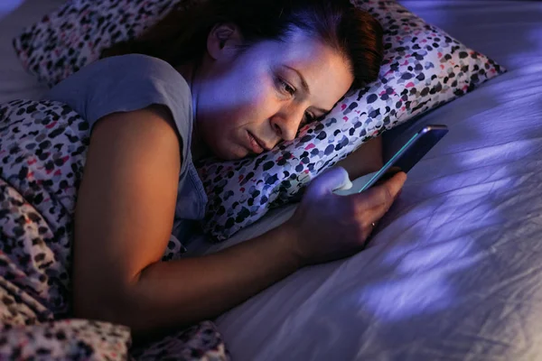 Young woman using smartphone in bed at night