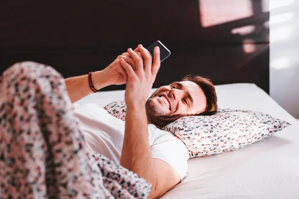 Young man using smartphone in bed in the morning