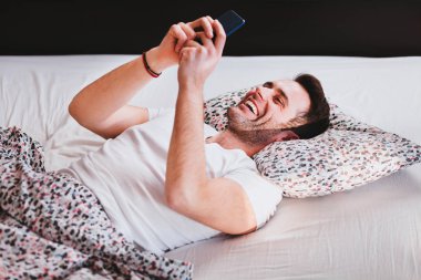 Sabahleyin yatakta Smartphone kullanan genç adam