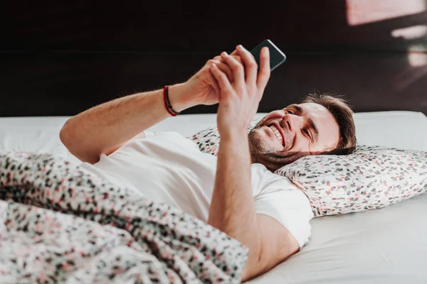 Young man using smartphone in bed in the morning
