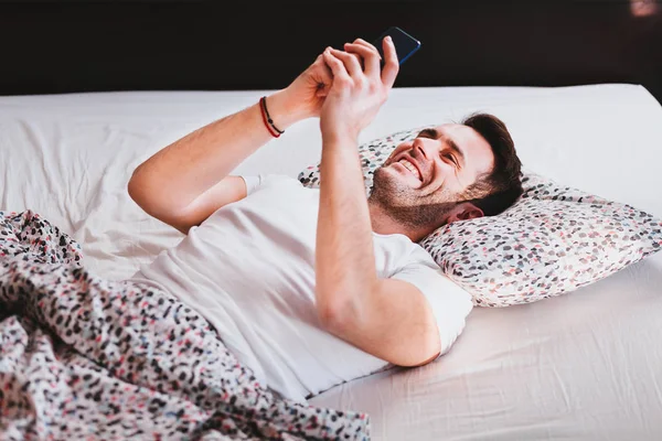 Young man using smartphone in bed in the morning