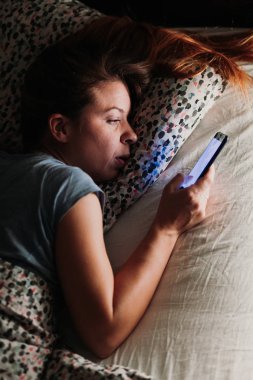 Geceleri yatakta Smartphone kullanan genç kadın