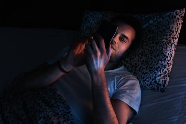 Geceleri yatakta Smartphone kullanan genç adam