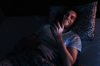Geceleri yatakta Smartphone kullanan genç adam