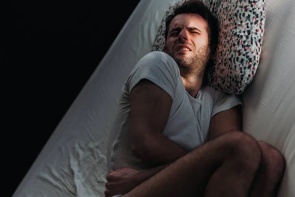 Young depressed man in pain on the bed