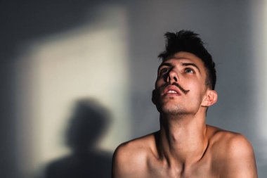 Umutsuzluk pencerenin yanındaki genç gömleksiz adam